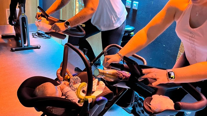 Three people on exercise bikes with a pram in between two of them 