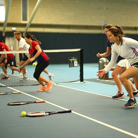 A group of people on a tennis court with racquets laid out in front of them. They are using the racquets as a marker for running drills