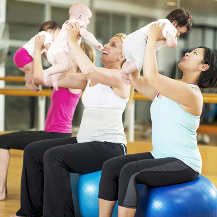 A group of adults sitting on exercise balls holding babies up. 