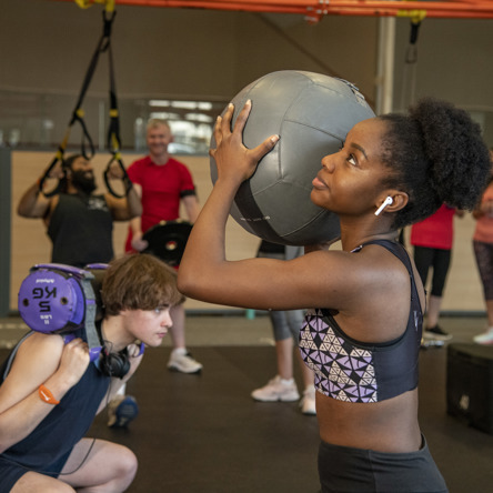 Group strength training, person in foreground with medicine ball raised 