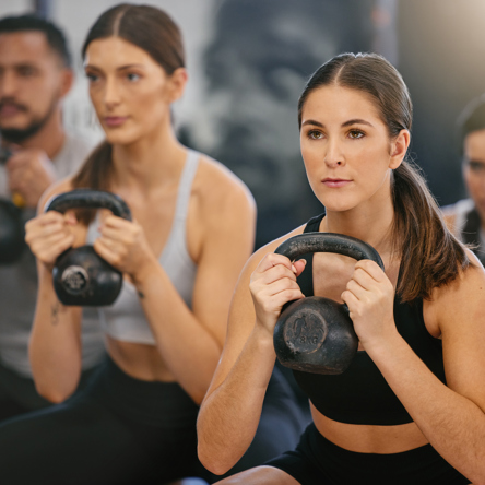 A group of adults squatting with a kettle bell during class