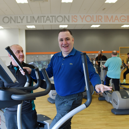 Person smiling on cross trainer with coach by their side 