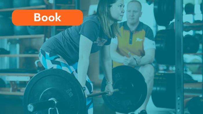 An instructor in a gym helping a woman perfect her barbell deadlift technique