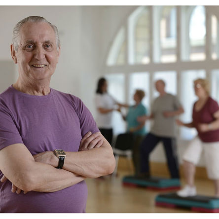 older person in foreground crossed arms smiling with group class behind him 