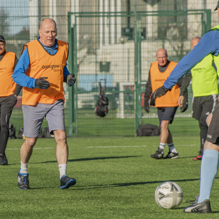 Group of people wearing colourful bibs with a football being passed 