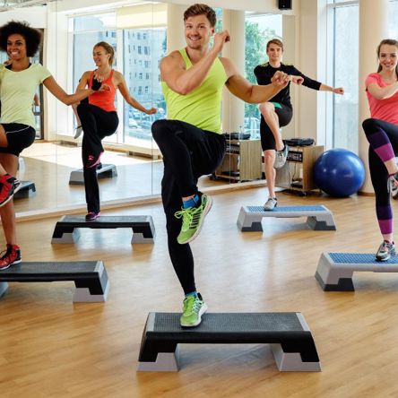 A group of people working out in a studio, by stepping up onto a fitness step (small platform)