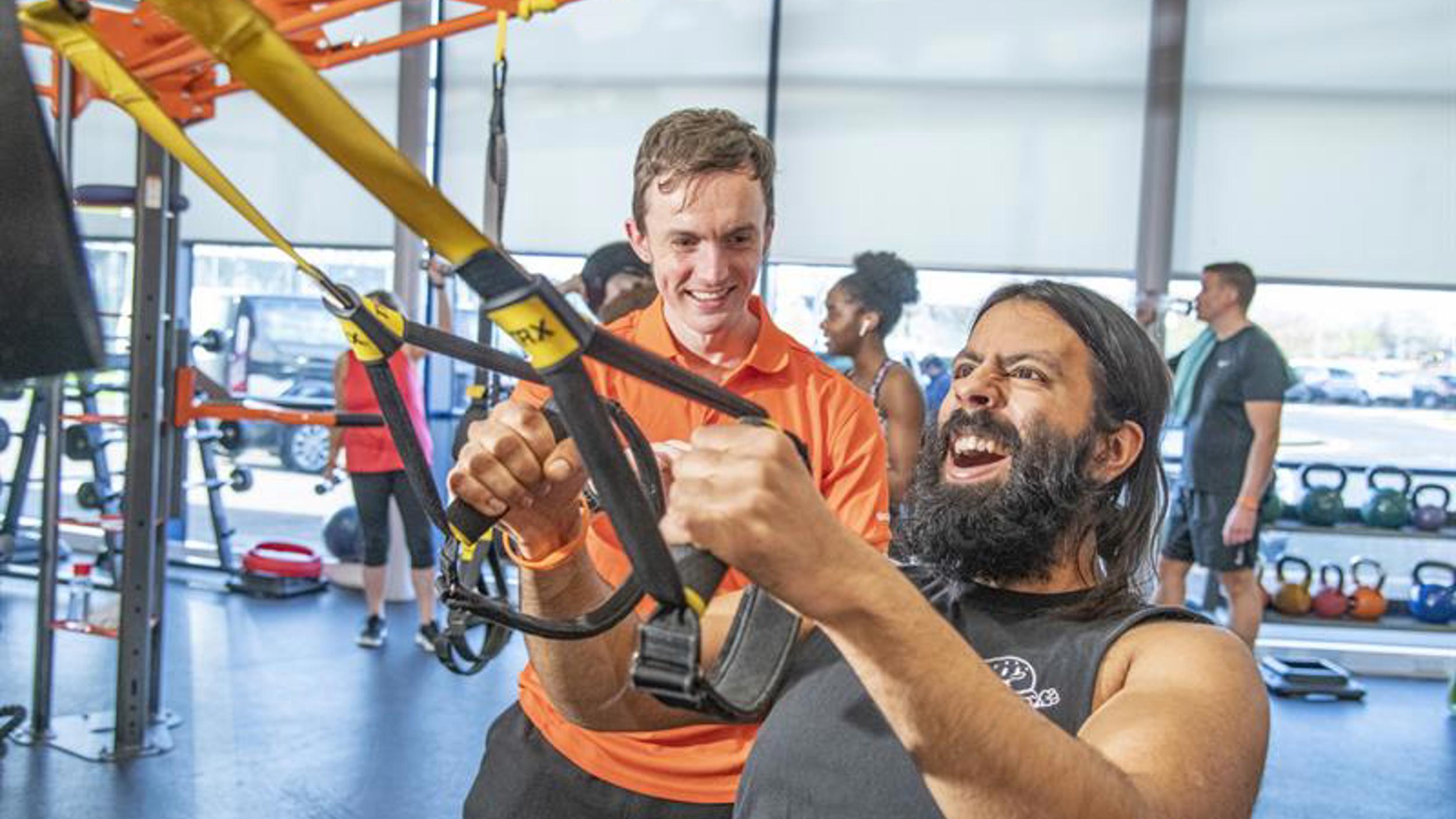 Someone working out in a gym using resistance bands while an instructor provides encouragement