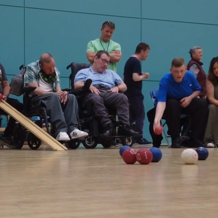 A group of people in a sports hall, some in wheelchairs, taking part in a game of Boccia