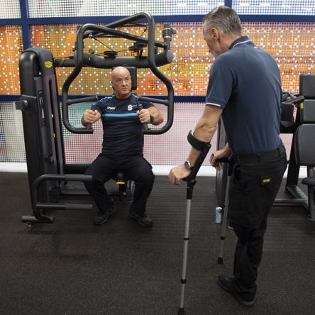 Coach in gym demonstrating equipment to person on crutches 