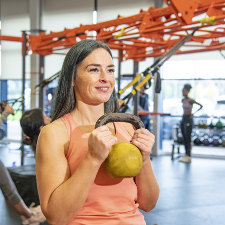 Person smiling, holding kettle bell to chest 