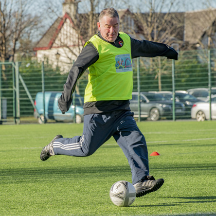 An older footballer wearing a yellow bib kicking ball