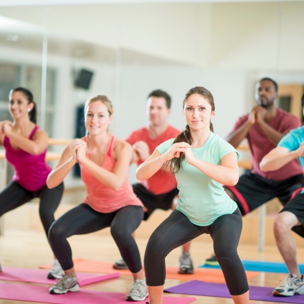 A group of people in a fitness studio, all doing squats as part of a fitness class