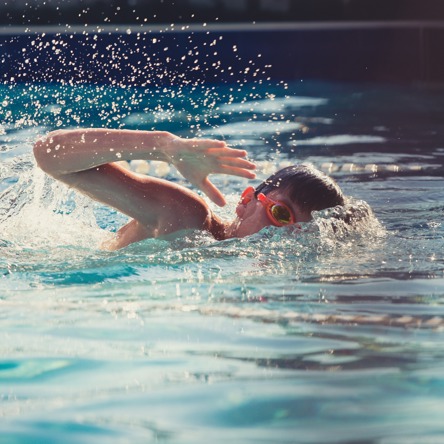 Child with goggles on doing forward crawls with arm mid-air 