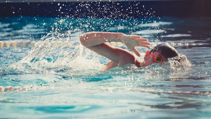 Child with goggles on doing forward crawls with arm mid-air