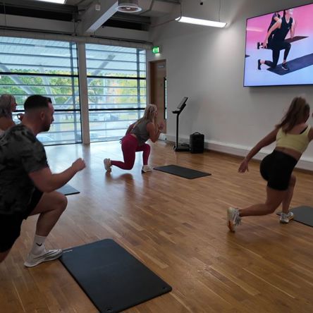 A group of people in a fitness studio following an on-screen virtual class