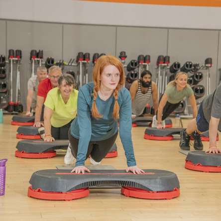 Group fitness class participants in a dance studio, all in a plank position on a fitness "step"