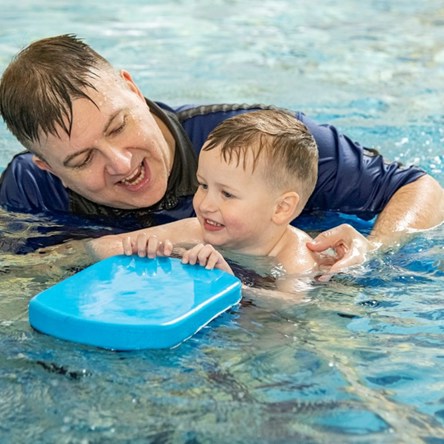 An adult swimming teacher teaching a young child to swim. The child is holding a float