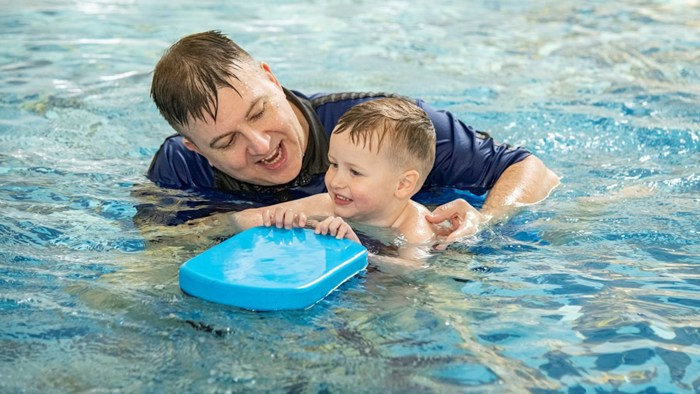 An adult swimming teacher teaching a young child to swim. The child is holding a float
