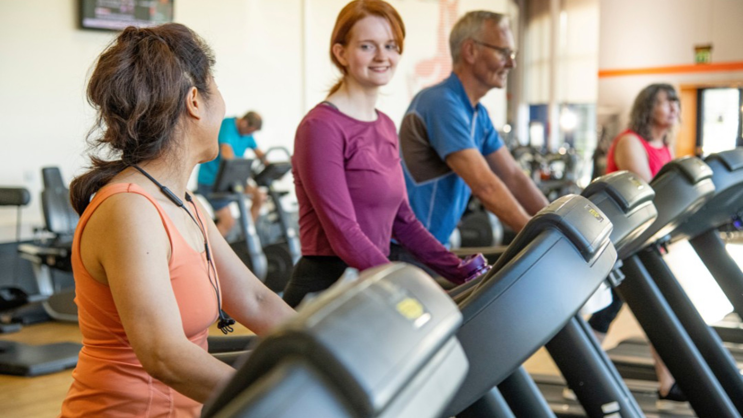 Three people working out while talking to each other on treadmills, side-by-side in a gym