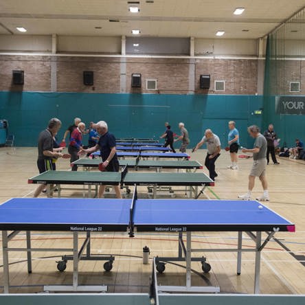 Gym hall with filled with table tennis tables and people playing