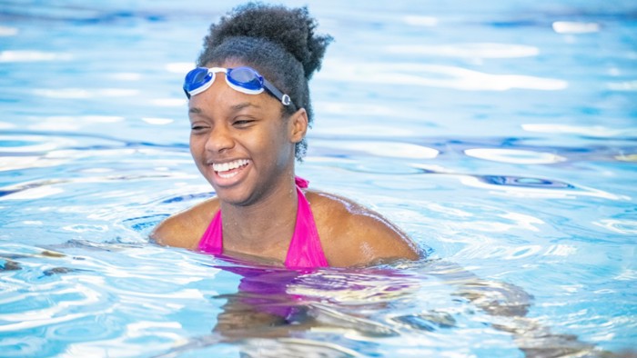 Someone relaxing and smiling in a swimming pool, wearing goggles pushed up onto their forehead