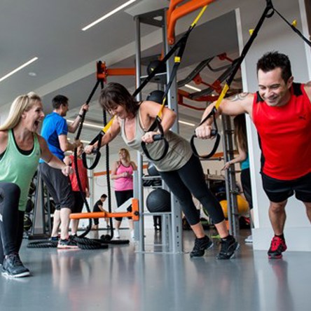 Group strength training, people using various kit and coach encouraging them 