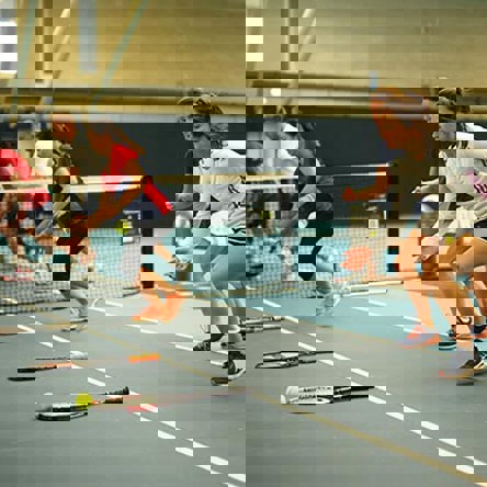 A group of people on a tennis court with racquets laid out in front of them. They are using the racquets as a marker for running drills