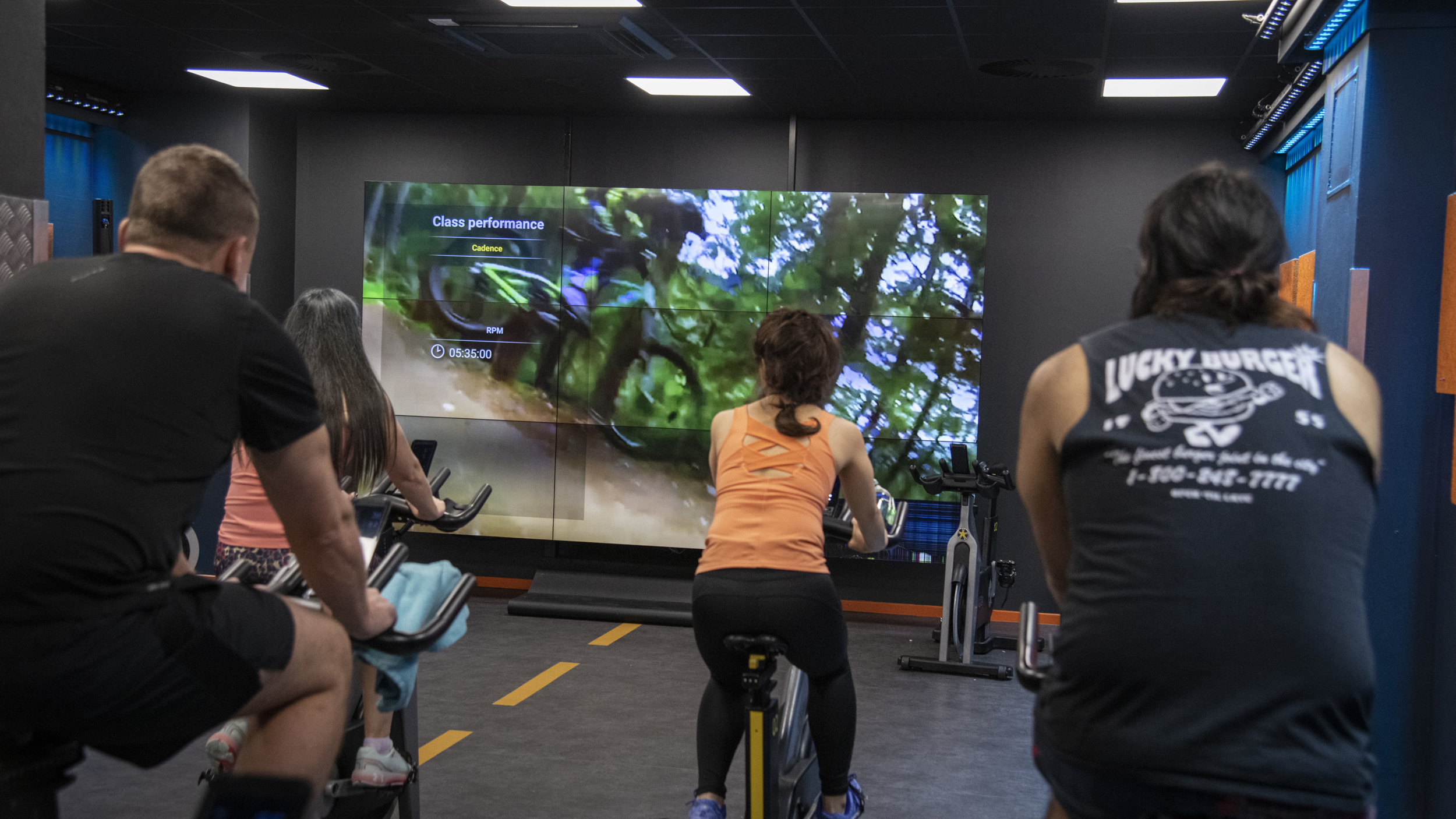 People shown in spin studio from behind with screen and bike route in front of them