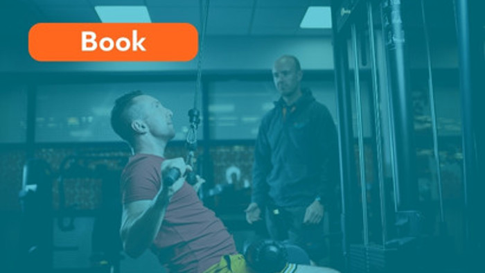 A gym instructor guiding a customer on how to use a cable resistance machine in a gym