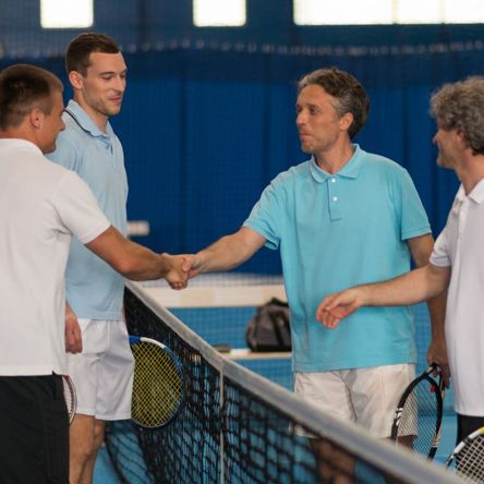 Four men holding tennis racquets and shaking hands over the net