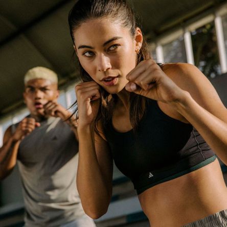 Two people holding their fists up like a fighter as they take part in a BODYCOMBAT class in a fitness studio
